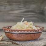 квашеная капуста в глиняной тарелке, рядом два зубчика чеснока