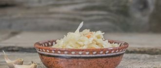 квашеная капуста в глиняной тарелке, рядом два зубчика чеснока