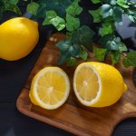 половинки лимона на разделочной доске, рядом целый лимон на столе с зеленой листвой