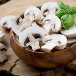 свеэие шампиньоны, нарезанные пластинками, в мисочке на пне