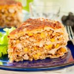 треугольный кусочек запеканки с курицей, овощами и кукурузой на тарелке с листьями салата